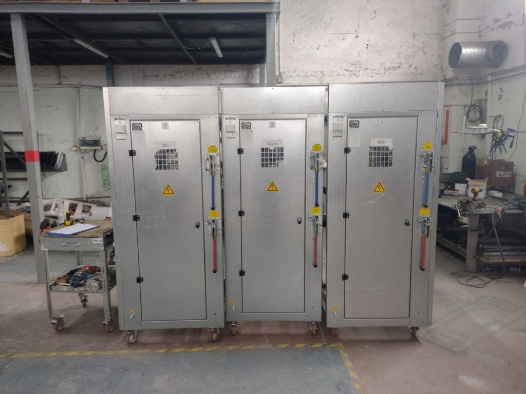 Three assembled switchgear cabinets with manual operating levers in production workshop